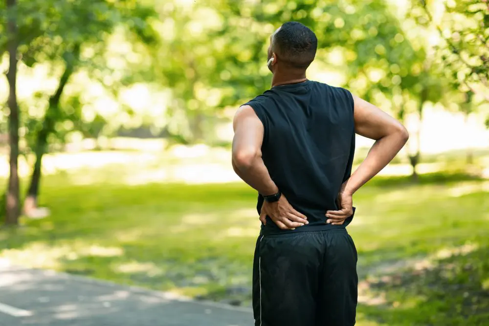 young male in the aprk holding his back due to pain