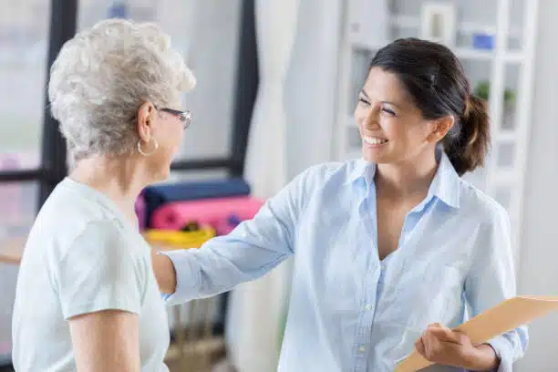 Cheerful mid adult Asian female chiropractor talks with new patient before beginning treatment.