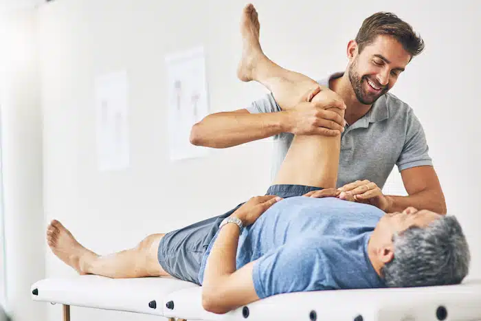 young male physiotherapist assisting a senior patient with leg adjustments